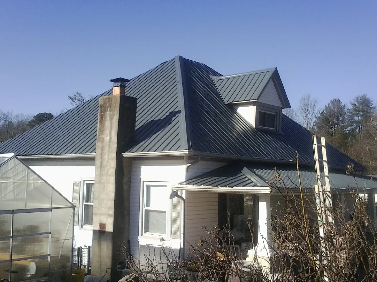 Dark blue standing seam metal roof on a white farmhouse with dormer — Slate & Tile Roof Repair by Roofing Brothers in Gobles