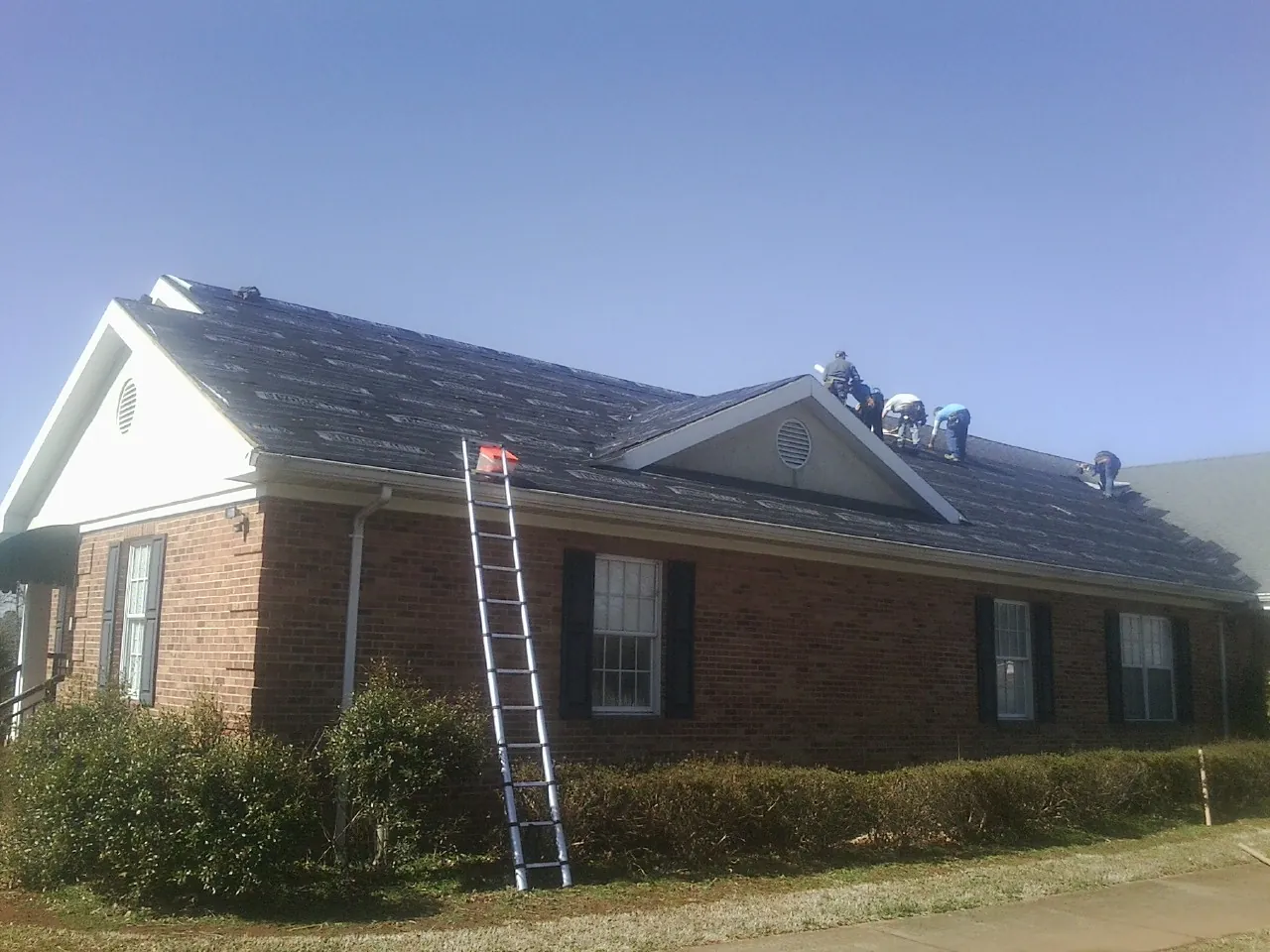 Crew tearing shingles off a brick ranch roof with a ladder set — Emergency Roof Repair work by our crew in Gobles