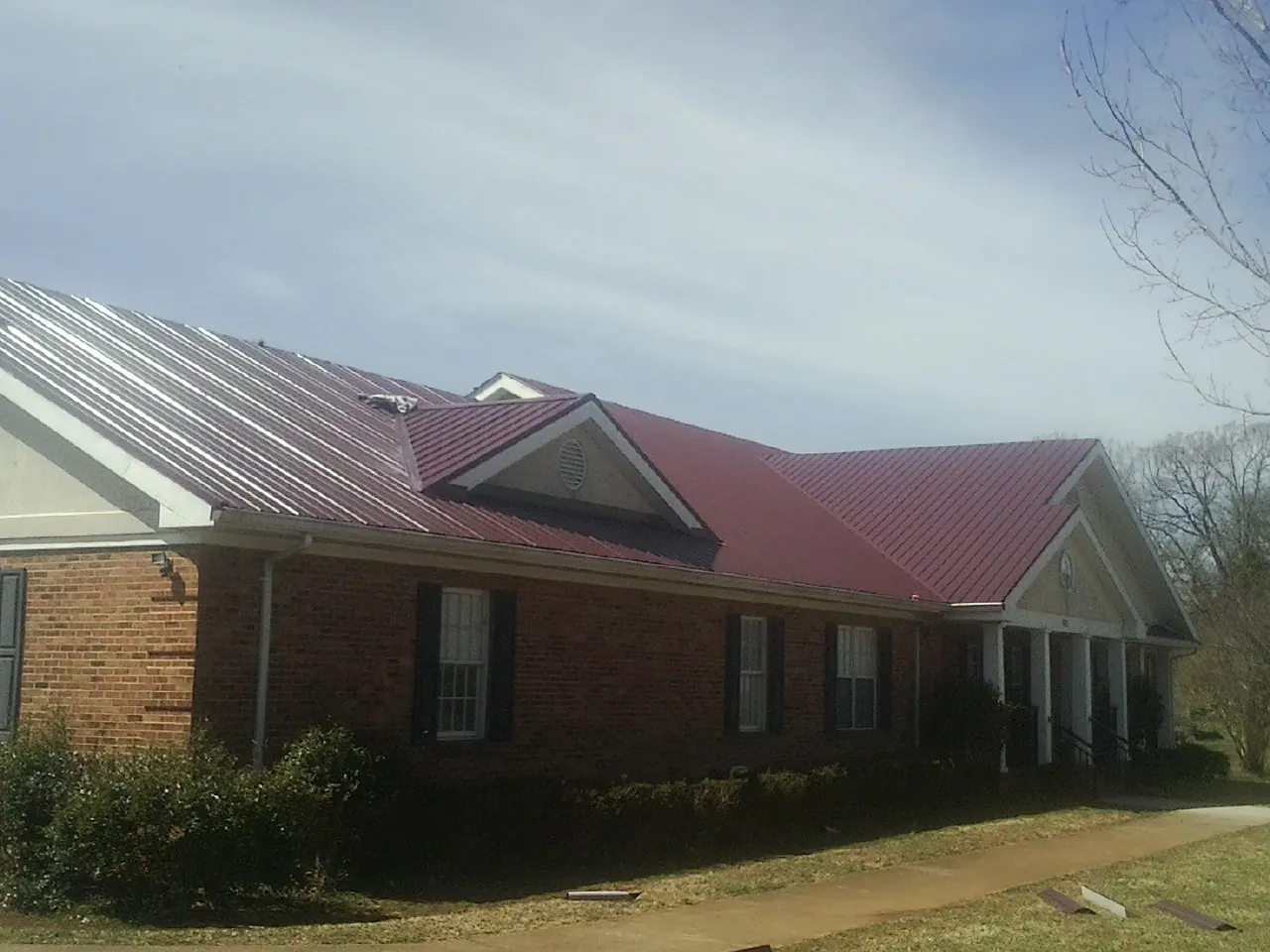 Red metal roof with gabled entries on a long brick building, from a Hail Damage Roof Repair job in Gobles