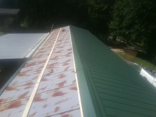 Old rusted panels beside newly installed green metal roofing — Wind Damage Roof Repair by Roofing Brothers in Gobles