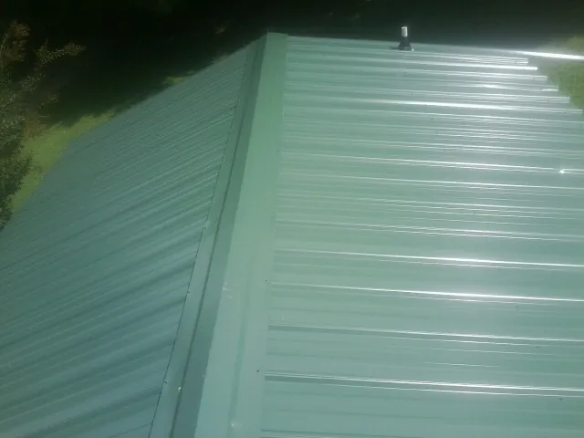 New green metal panels meeting at the ridge of a roof — Flat Roof Repair work by our crew in Gobles