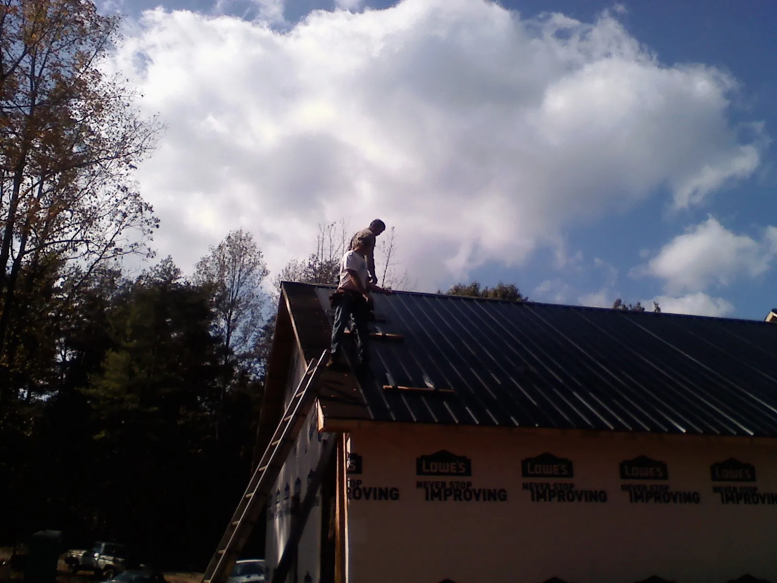 Roofer fastening dark metal panels high against a cloudy sky, from a Roof Inspection job in Gobles